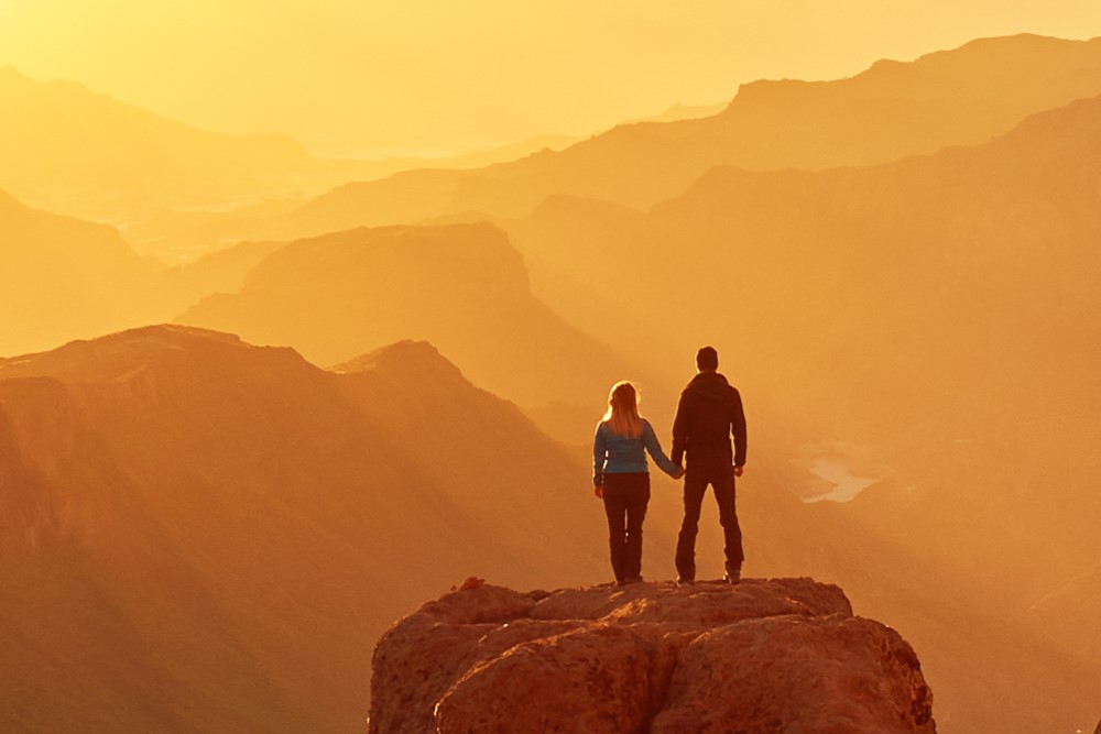 Two people watch the sunset over the mountains