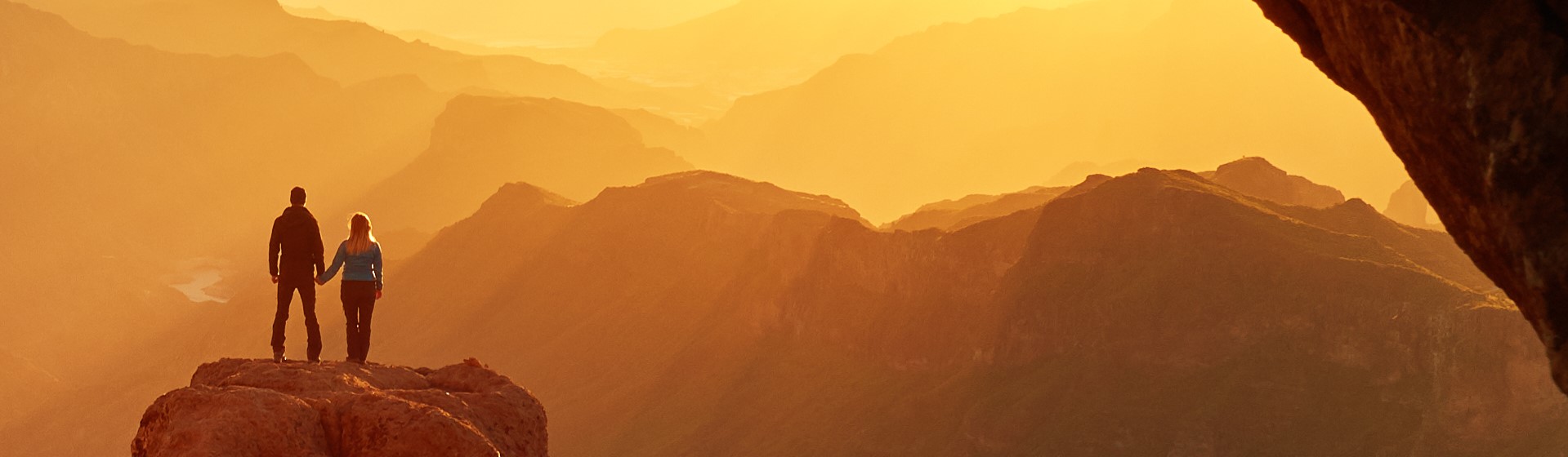 Two people watch the sunset over the mountains