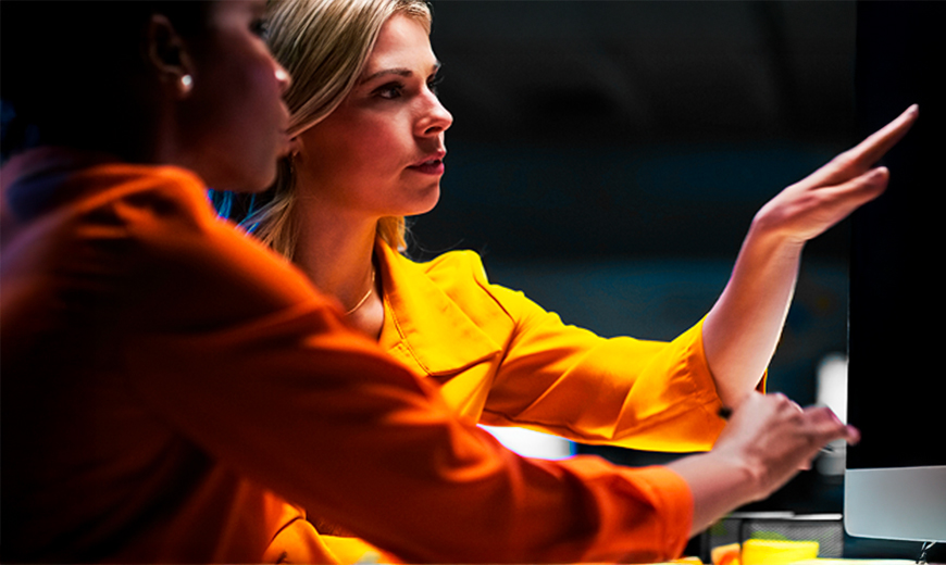 Two colleagues reviewing data and digital dashboards on a screen in a collaborative tech workspace