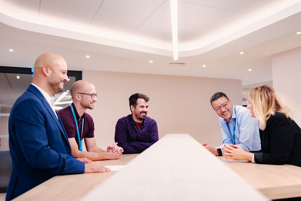 A group of SCOR employees engaged in friendly discussion in a meeting room, illustrating their commitment and expertise in reinsurance, data, and finance