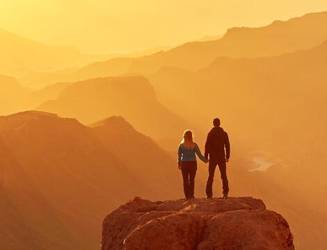 Two people watch the sunset over the mountains