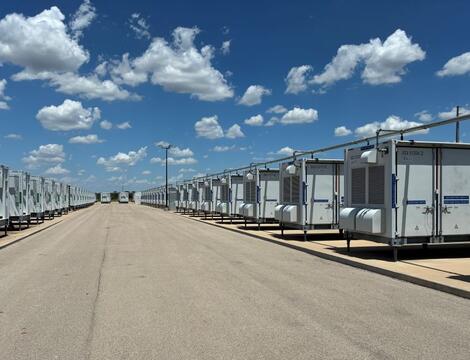 Battery energy storage units on each side of a road, blue sky dotted with clouds