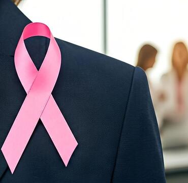 Breast cancer ribbon on a woman's jacket with colleagues in the background