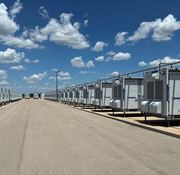 Battery energy storage units on each side of a road, blue sky dotted with clouds
