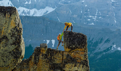 Mountain climber helping another to reach the summit