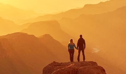 Two people watch the sunset over the mountains