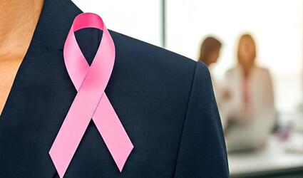 Breast cancer ribbon on a woman's jacket with colleagues in the background