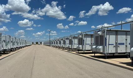 Battery energy storage units on each side of a road, blue sky dotted with clouds